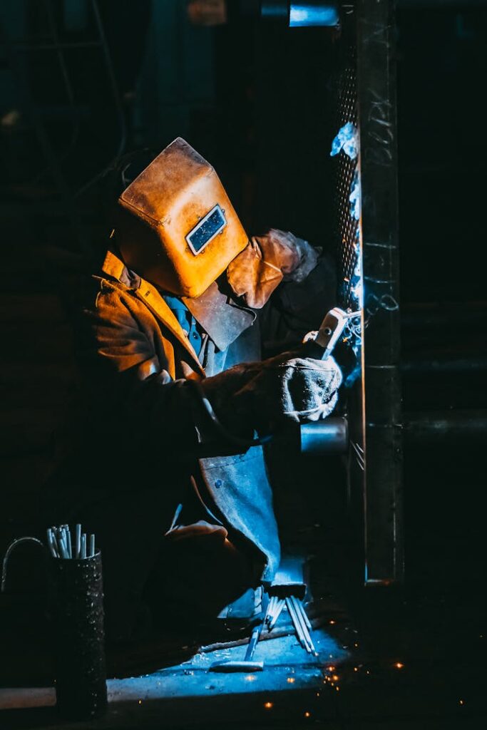 pexels photo 2760343 A welder wearing safety gear sparks metal in a dimly lit industrial setting.