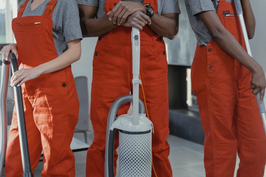 pexels photo 6195129 Three workers in red coveralls with cleaning tools in a room.